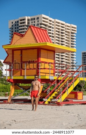 Young male tourist with a well-groomed body, having his picture taken at one of the lifeguard booths in Miami beach, on a beautiful sunny day.