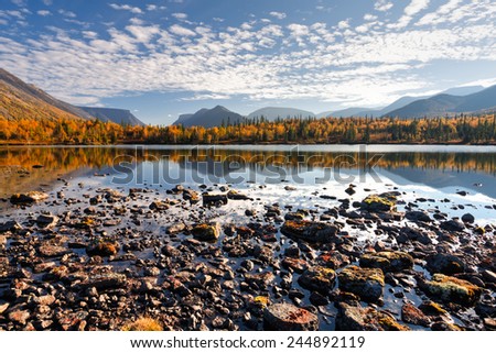 Iconic Hibiny mountains landscape with cloudy evening sky and bright colorful taiga forest reflected in shallow Polygonal lake, Russia above the Arctic circle