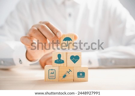 Hand holding a wooden block adorned with healthcare and medical icons. Depicting safety and health, symbolizing pharmacy, family care, and heart well-being. A concept of happiness.