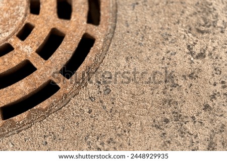 A rusty iron hatch with a pattern above an observation well is located on auto road in daytime. Close-up