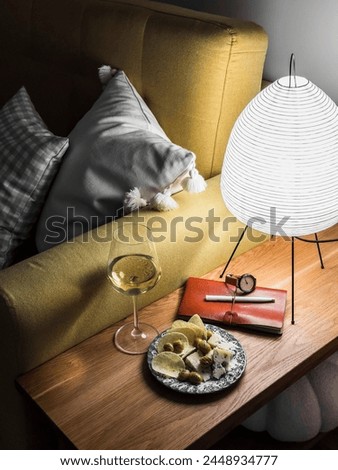 Homemade aperitif in a cozy evening living room - a glass of white wine, a plate with chips, cheese and olives on a wooden table next to the sofa Royalty-Free Stock Photo #2448934777