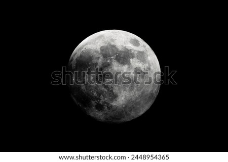 A black and white photograph showcasing the full moon in the midnight sky, against a dark black background. The astronomical object shines brightly, casting moonlight over the world Royalty-Free Stock Photo #2448954365
