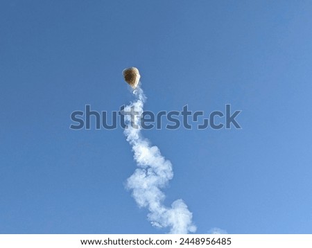 Photo of a hot air balloon carrying a series of firecrackers on its lower side tied with string and exploding while flying.