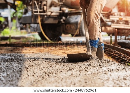 man is working on a construction site, using a shovel to move gravel. The scene is set in a rural area, with a truck in the background. Scene is hard work and determination