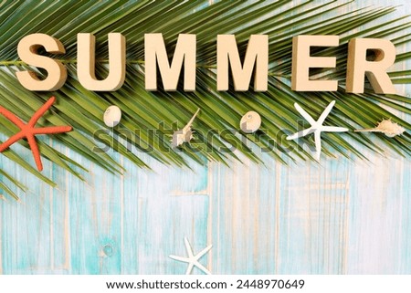 Composition seen from above on a wooden background of turquoise boards with letters forming the word Summer on palm leaf and starfish. Summer vacation concept.