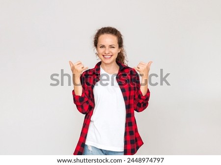 Cheerful woman wearing casual outfit smiles and gestures Shaka sign in front of plain background.