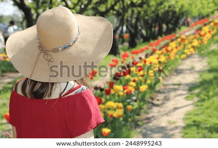 Young girl with wide  straw boater hat in the field of Tulips in Royalty-Free Stock Photo #2448995243