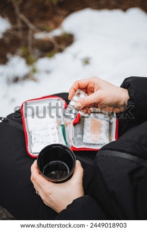 Female hands holding a glass of water and pills while sitting on the snow, a travel first-aid kit, medications for stomach pain. High quality photo