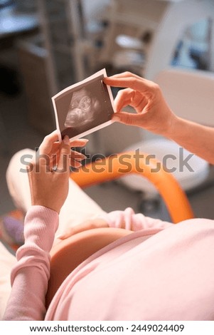 Unrecognizable pregnant woman visiting doctor and looking at ultrasound photo