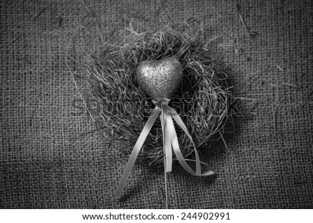 Black and white photo of decorative heart lying in birds nest 