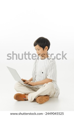 Happy Asian little boy sitting typing laptop isolated on white background, online learning concept, Looking at camera and full body composition.
