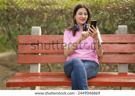 Happy adult woman using headphones and smart phone listening to music in a summer park