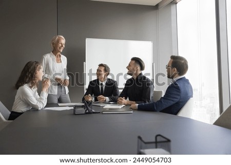 Happy business team having pleasant talk in contemporary board-room. Seminar or corporate training event led by smiling mature 50s business coach, share knowledge, explain strategy to staff members Royalty-Free Stock Photo #2449054703
