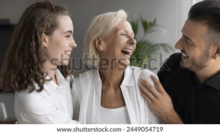 Happy Mothers Day celebration, adult siblings congratulate their happy mom with holiday, hugging, feeling love, showing support. Three male female companions colleagues enjoy joint success in office Royalty-Free Stock Photo #2449054719
