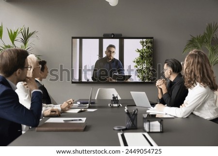 Arabic businessman speaker hold video conference for staff using application. Group of interested business people, employees listening speech, information, opinion of male boss shown on monitor screen Royalty-Free Stock Photo #2449054725