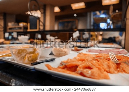 Buffet spread with citrus dessert and sliced salmon on white plate in warm, inviting restaurant or dining area with out of focus background dishes and bar area.