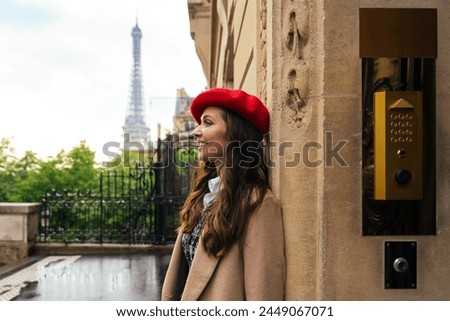 Beautiful young woman visiting Paris. Parisian girl with red hat and fashionable clothes having fun in the city center and landmarks area. Tourist looking ahead with Eiffel tower in the background