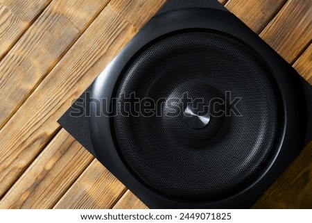 Large cubic subwoofer in a wooden enclosure with metal grille on a background of natural pine boards. Audiophile concept. Natural style. Close-up Royalty-Free Stock Photo #2449071825