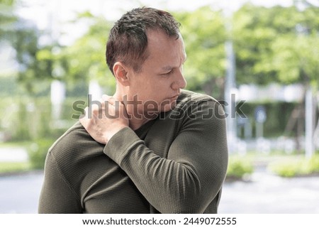Middle aged asian man suffering from shoulder pain, shoulder injury, shoulder stiffness symptoms  with office syndrome or overwork Royalty-Free Stock Photo #2449072555