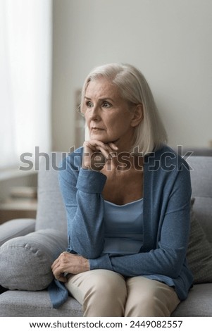 Pensive senior woman spend time at home, sit on sofa, look in distance, suffer from anxiety, having psychological problem, miss, recollect past, worrying about health. Melancholy, nostalgia, solitude Royalty-Free Stock Photo #2449082557