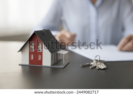Female property buyer sign contract, make deal, accept agreement, take bank mortgage for home purchase, close up view to keys and small miniature of cottage house on desk. Real-estate selling services