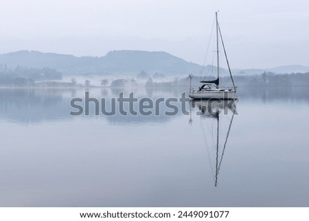 Stunning peaceful landscape image of misty Spring morning over Windermere in Lake District with boats moored on lake and distant misty peaks