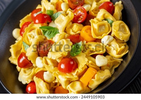 tortellini salad with cherry tomatoes, mini mozzarella, fresh basil leaves in black bowl, dutch angle view, close-up Royalty-Free Stock Photo #2449105903