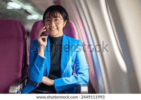 A joyful passenger in a yellow blazer drinks coffee and uses her smartphone on a bright airplane.