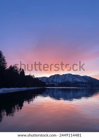 A beautiful sunset in Lake Tahoe California reflects off the calm water. Many colors illuminate the sky behind the mountain and forest landscape.