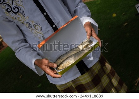 Asian adult Muslim men carrying boxes of presto milkfish in packaging ready for consumption, sharing during Eid al-Fitr.