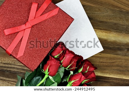 Gift box with long stem red roses and card over an old wooden background with room for copyspace.