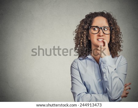 Closeup portrait nervous woman with glasses biting her fingernails craving for something, anxious isolated grey wall background with copy space. Negative human emotion, facial expression body language Royalty-Free Stock Photo #244913473