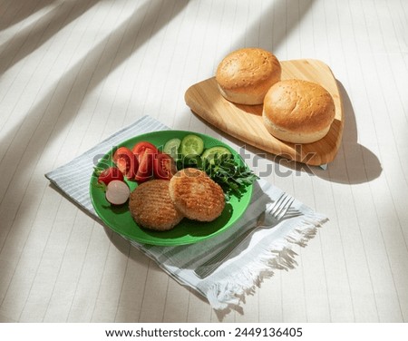 Two fried cutlets on a plate with fresh vegetables, with hamburger buns