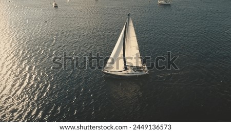 Aerial sun light above sea surface with sail boat. Yacht cruising at serene waterfront. Summer vacation scenery of yachting at open ocean bay. Ship sailing on wind wheather. Cinematic drone shot