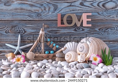 The letters of the word Love, a seashell and a decorative driftwood ship on a sea pebble beach. Marine decorations. Handmade work. Blue wooden background.