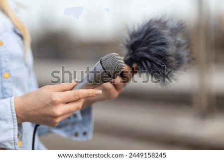 Female reporter journalist on the spot, holding microphone and dictaphone sound recorder with wind protector