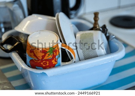 Clean dishes - cups, plates, bowls, cooking pot are getting dry in the broken blue washbowl at the camping kitchen. Drying utensils on the kitchen  counter. selective focus Royalty-Free Stock Photo #2449166921