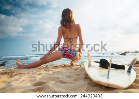 Young lady surfer warming up on the beach before surfing