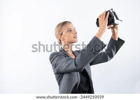 Caucasian business woman holding VR glass while standing at white background. Professional project manager looking visual reality goggle while wearing suit. Innovation technology concept. Contraption.