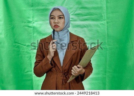cute asian woman wearing hijab and blazer concentrated on thinking notes planning to creating strategy over green background