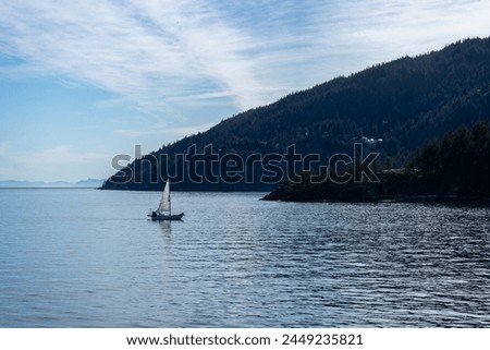 Rule of thirds sailboat in calm water just off the coast of green, forested Bowen Island, British Columbia, Canada