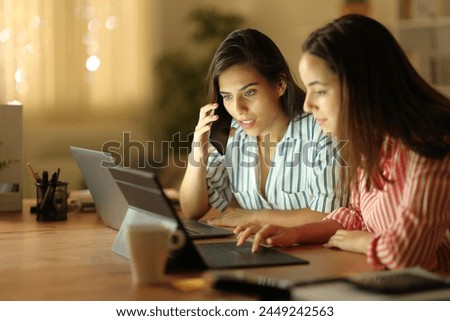 Two tele workers talking on phone solving online problem in the night at home Royalty-Free Stock Photo #2449242563