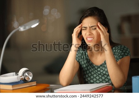 Stressed student suffering head ache in the night at home Royalty-Free Stock Photo #2449242577