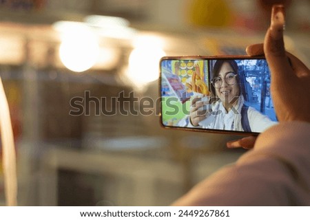 Photograph of a tourist woman shopping, smiling and taking a selfie with her cell phone, at a stall selling traditional churros and Mexican snacks on the street, during her trip