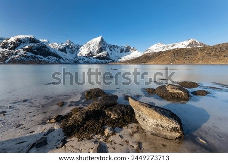 Sunny winterday with sea and mountains in the background - longtime exposure - Lofoten Island, Norway Royalty-Free Stock Photo #2449273713