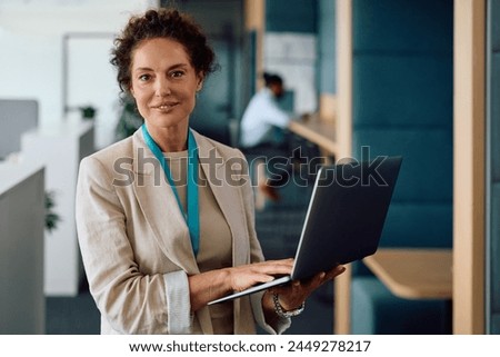 Smiling businesswoman using laptop while working at corporate office and looking at camera.