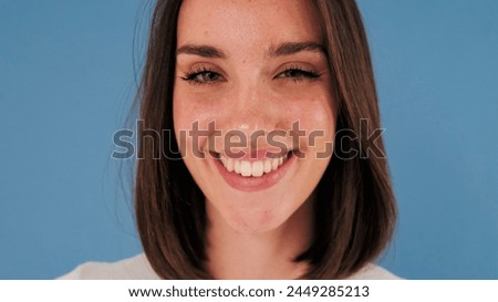 Close-up portrait of young woman looking at camera with smile, isolated on blue background