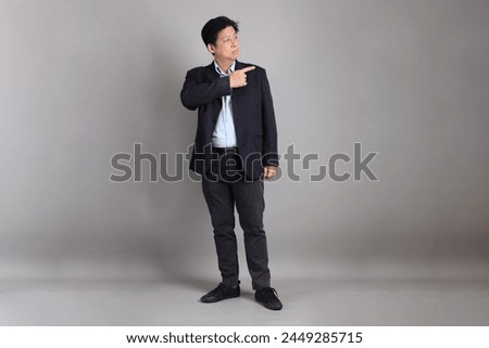 The Asian Businessman with formal dressed with gesture of pointing on the gray background.