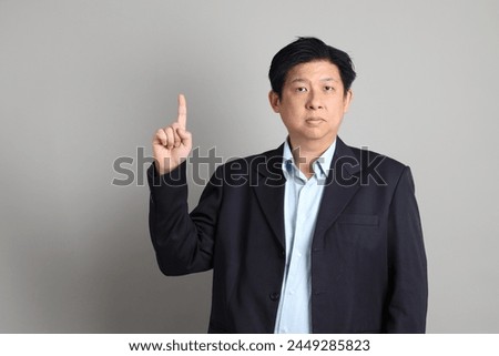The Asian Businessman with formal dressed with gesture of pointing on the gray background.