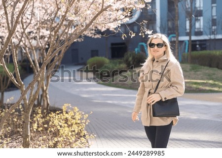 Blonde touches a branch of blooming cherry standing in the park